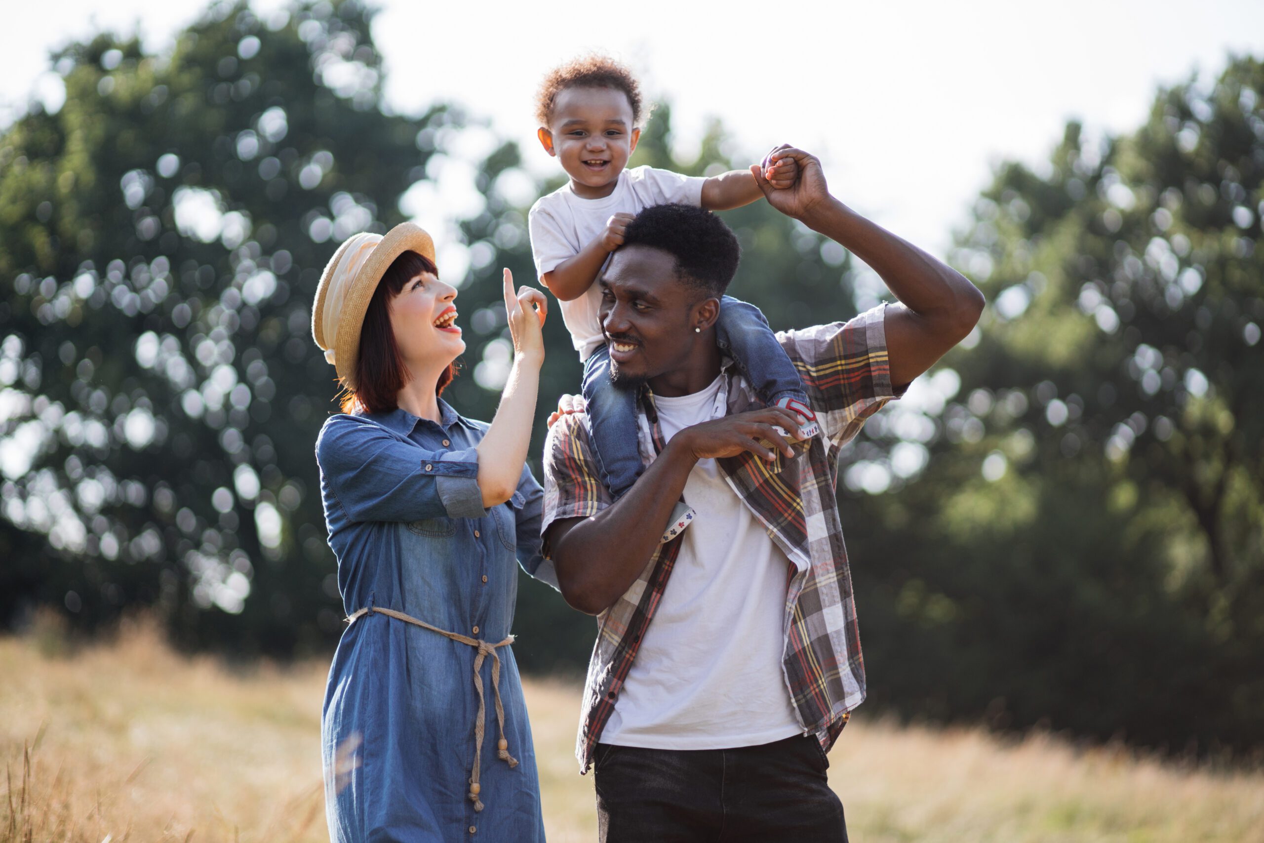 Boy sitting on father's shoulders and smiling to mother